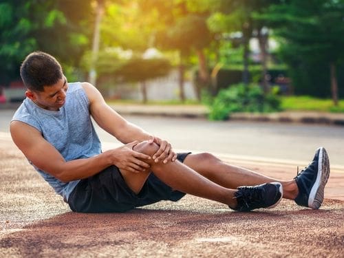 Sono principalmente due le cause delle lesioni del menisco: scoprile ora! Uomo seduto sul pavimento si tocca il ginocchio dolorante
