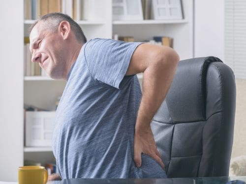 Uomo si tocca la schiena dolorante mentre è seduto alla scrivania