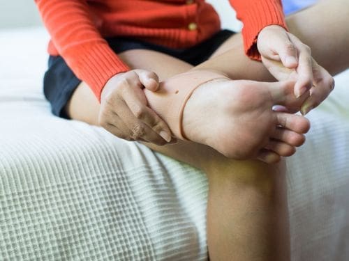 Scopri cos'è una tendinite al piede. Donna si tocca il piede a causa di un dolore.